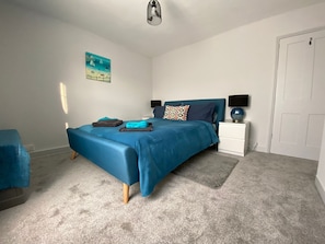 A bedroom with a bed, a nightstand, a lamp, a painting, and a door.