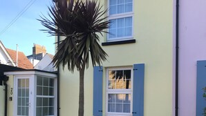 A two-story house with a yellow facade, blue shutters, and a small garden area with a palm tree. - Just a stone’s throw from the beach (Walmer)