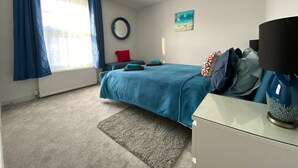A bedroom with a bed, a nightstand, a lamp, a round mirror, and a painting on the wall. - Just a stone’s throw from the beach (Walmer)