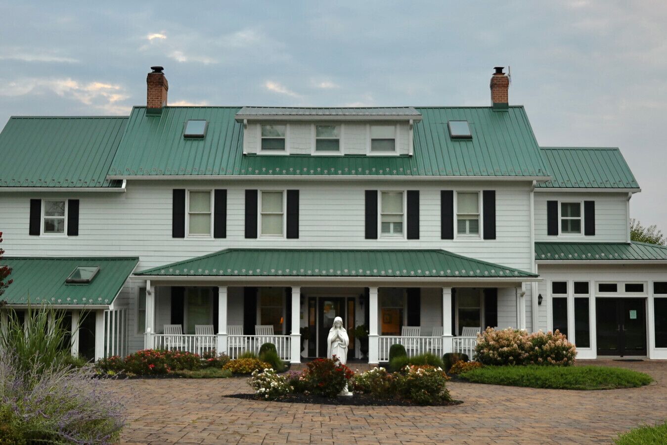 A large, two-story building with a green roof and white exterior. It features a covered front porch with white railings and a statue in front.