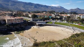 Un poble costaner amb una platja, una construcció que sembla un castell i muntanyes al fons.