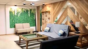 A modern room with a sofa, a bed, a glass coffee table, and a green wall with foliage. - Spacious Home- Centrally located near St. Paul  (Little Canada)