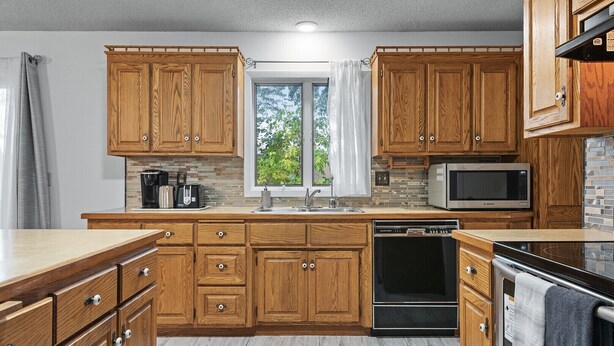 A kitchen with wooden cabinets, a Bosch microwave, a dishwasher, and a window with a view of greenery. - Spacious Home- Centrally located near St. Paul  (Little Canada)