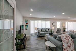 A spacious living room with a grey sofa, a coffee table, and a dining area with a bench.