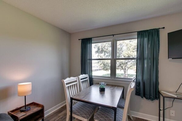 A dining area with a table and chairs, a lamp, and a window with curtains.