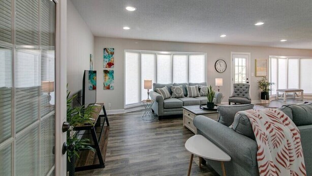 A spacious living room with a grey sofa, a coffee table, and a dining area with a wooden table and chairs.