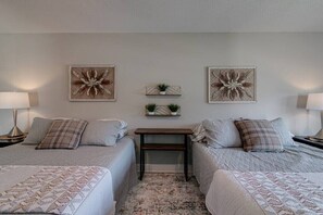 Une chambre avec deux lits, une table de chevet avec une lampe, une petite table avec une plante et deux tableaux représentant des fleurs, accrochés au mur.