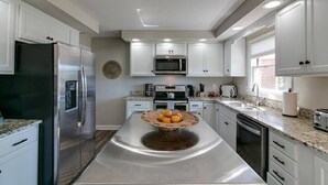 A modern kitchen with white cabinets, stainless steel appliances, and a central island with a woven basket.