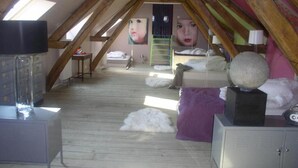 Ein Schlafzimmer im Dachgeschoss mit geneigten Holzbalken, einem Schlafplatz in der Mansarde, einem Schrank und einem großen Spiegel.