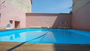 Ein klares, blaues Schwimmbecken mit Metallleitern, umgeben von einer Holzterrasse und rosafarbenen Wänden.