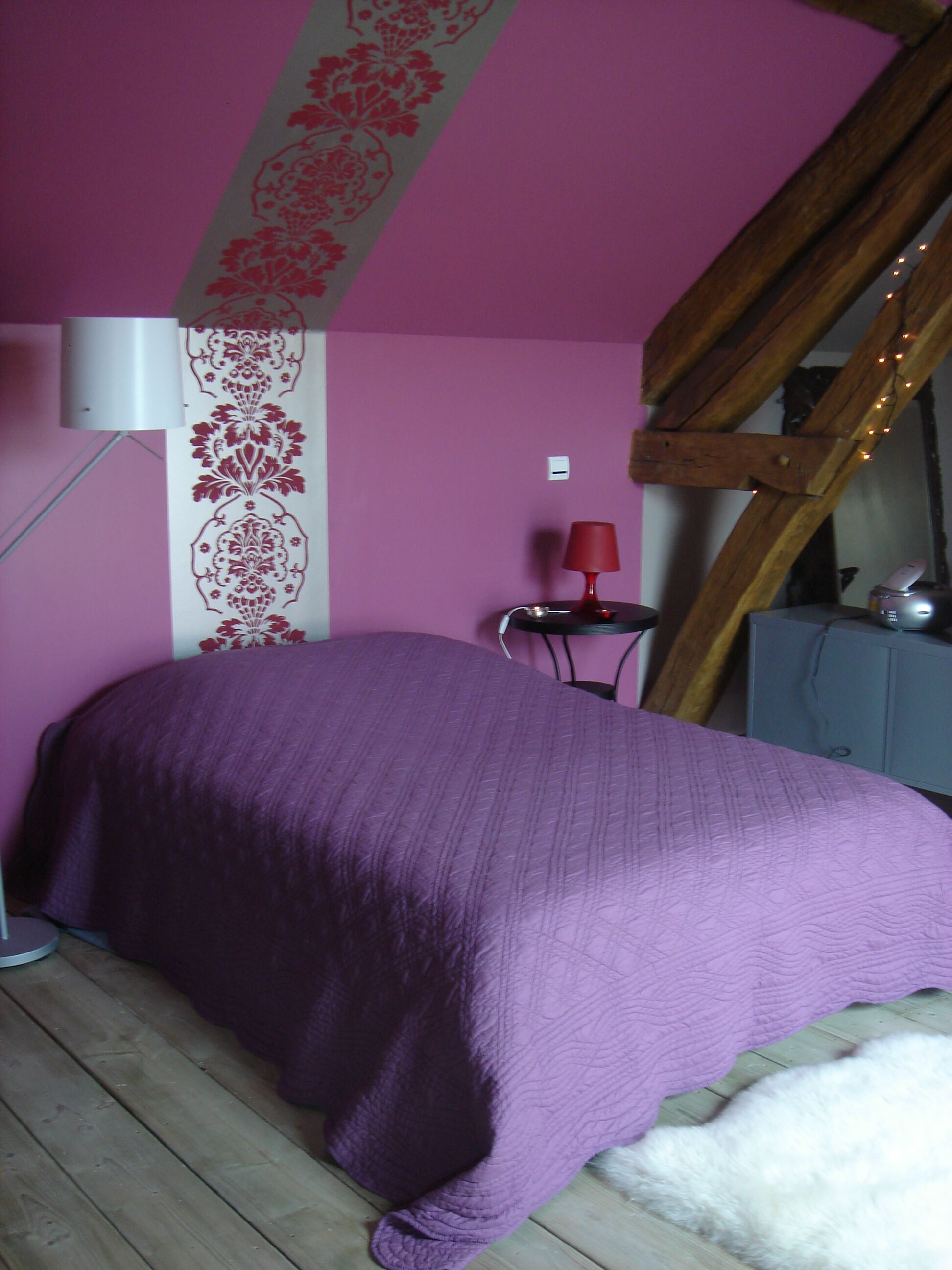 Een slaapkamer met een paars dekbed, een rode lamp en een houten ladder.