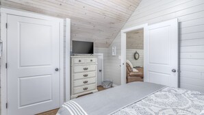A bedroom with a bed, dresser, television, and a door leading to another room.