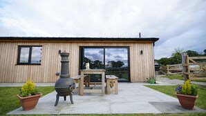 A wooden building with a large window, a patio with a table and chairs, and two potted plants.