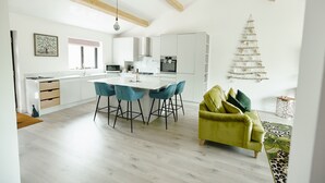 A modern kitchen with white cabinets, a central island with bar stools, and a green sofa in a living area.