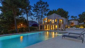 Une maison moderne à deux étages, dotée d’une piscine, d’un espace salon extérieur et d’un balcon bien éclairé.