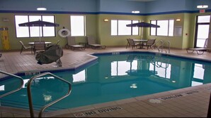 Une piscine intérieure avec des chaises longues, des parasols et un panneau indiquant « Il est interdit de plonger ».