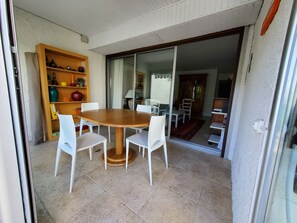 Zona pranzo con tavolo in legno e sedie bianche, una libreria con diversi oggetti e una porta scorrevole in vetro che dà su un'altra stanza.