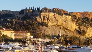 A marina with boats docked, a building with a balcony, and a hill with ruins in the background. -  LOVELY APART 2 BEDROOMS FOR 5-GARDEN GARAGE NEAR BEACHES PORT AND CITY CENTER (Cassis)