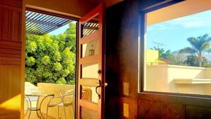An open door leading to a balcony with a table and chairs, a view of greenery, and a clear sky. - Villas San Ángel (Departamento) (Ajijic)