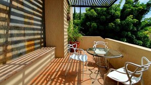 A patio with a glass table and white chairs, surrounded by a beige wall and potted plants. - Villas San Ángel (Departamento) (Ajijic)