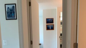 Un couloir aux murs blancs, doté d’un sol carrelé et de deux portes donnant sur d’autres pièces. Deux tableaux encadrés ornent le mur.