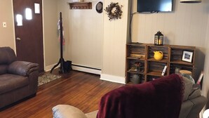 Ein Wohnzimmer mit braunem Ledersofa, einem roten Sessel, einer Holzbibliothek, einem Fernseher und einem dekorativen Kranz an der Wand.