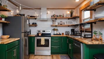 Een moderne keuken met groene kastjes, roestvrijstalen apparatuur, houten aanrechtbladen en diverse keukenspullen op planken.