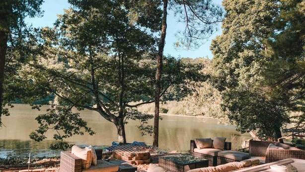Un área de estar al aire libre con mobiliario de mimbre y un jacuzzi junto a un lago.