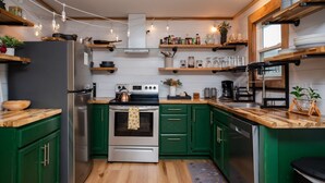 Una cocina moderna con armarios verdes, electrodomésticos de acero inoxidable, encimeras de madera y diversos utensilios de cocina en estantes.