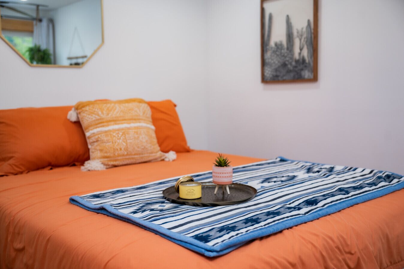 A bed with orange bedding, a blue and white striped blanket, a small potted plant, and a tray with a candle and a jar.