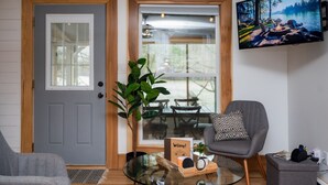 Una sala de estar acogedora con un sofá gris, una mesa de centro de vidrio, un sillón gris y un televisor montado en la pared.