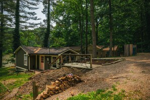 A rustic cabin with a porch, surrounded by a forest.