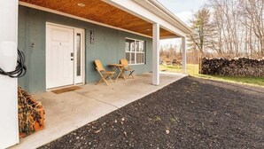 A covered porch with a concrete floor, a white door, and two wooden chairs.
