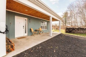 A covered porch with a concrete floor, a white door, and two wooden chairs.