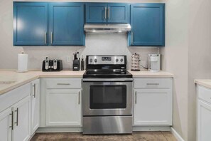 A kitchen with blue cabinets, a stainless steel stove, and white countertops.