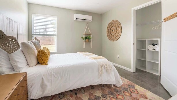 A bedroom with a bed, a hanging plant, a wall-mounted air conditioner, and a closet.