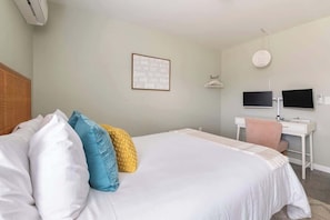 A hotel room with a bed, a desk, a chair, a TV, and a wall-mounted air conditioner. - Boho House- A Rural Escape with Fire Pit, EV, WFH (Ithaca)