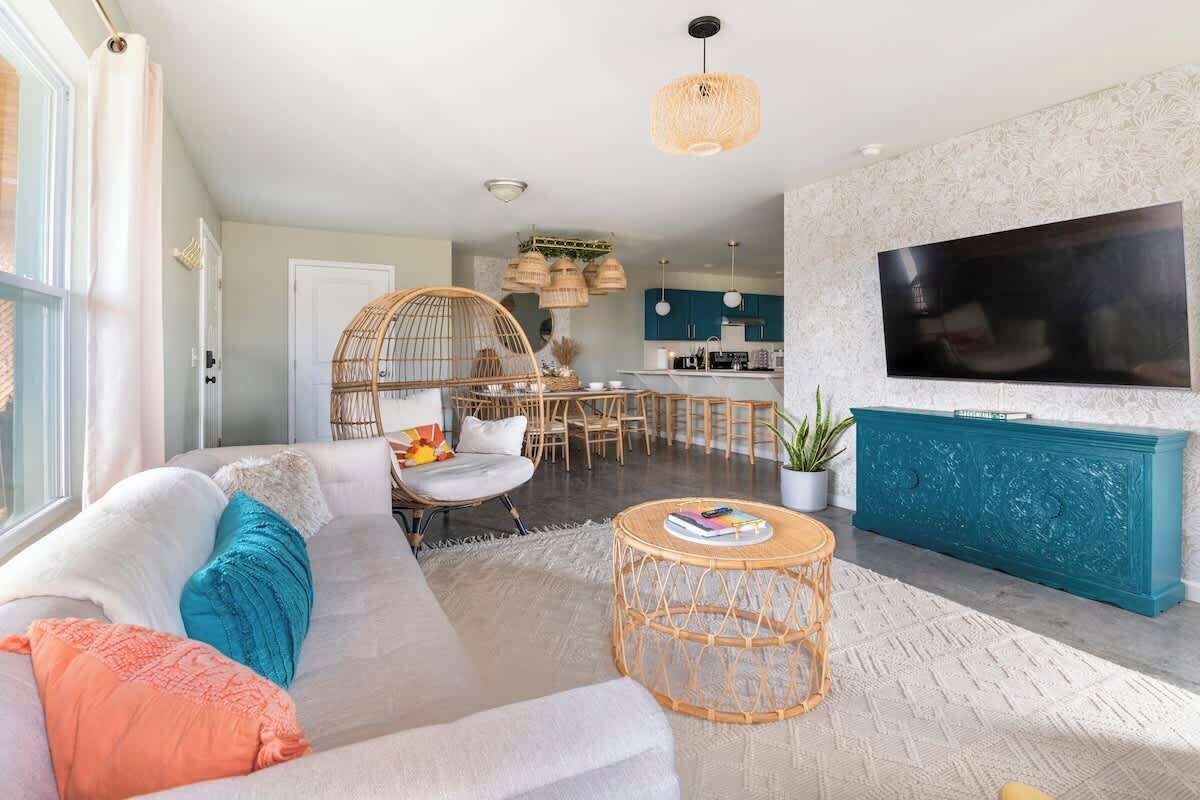 A living room with a sofa, a coffee table, a TV, and a dining area with chairs and a hanging light fixture.