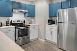 A kitchen with blue cabinets, a stainless steel refrigerator, a microwave, and a stove. - Boho House- A Rural Escape with Fire Pit, EV, WFH (Ithaca)