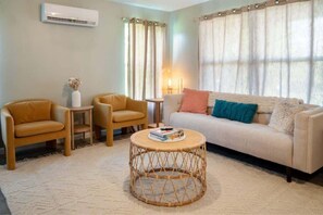A living room with a sofa, two armchairs, a round coffee table, a small side table, and a wall-mounted air conditioner. - Boho House- A Rural Escape with Fire Pit, EV, WFH (Ithaca)