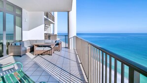 A balcony with a view of the ocean, a dining table, and wicker furniture. - The Oasis 2105 | Spacious, Lazy River, Poolside Grill, New Splash Pad, Pool with Slide! (Orange Beach)