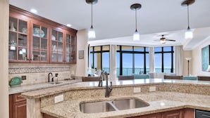 A modern kitchen with granite countertops, a stainless steel sink, and wooden cabinets. There are pendant lights and a ceiling fan. - The Oasis 2105 | Spacious, Lazy River, Poolside Grill, New Splash Pad, Pool with Slide! (Orange Beach)