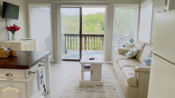 A spacious living area with a ceiling fan, a kitchen with white cabinetry, a dining table, and a sofa. - Comfortable and affordable condo in four seasons. Monthly Discount Available. (Village of Four Seasons)