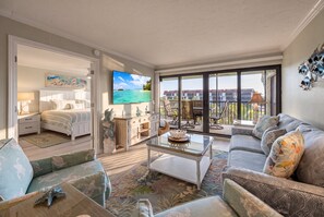 A spacious living area with a balcony, a large flat-screen TV, and a comfortable seating arrangement.