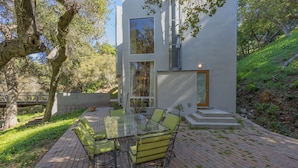 A modern house with a glass dining table and chairs, surrounded by a brick patio and greenery.