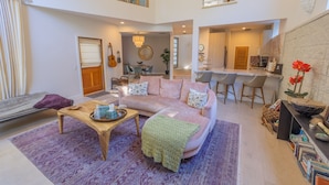 A spacious living area with a high ceiling, a cozy seating arrangement, and a kitchen area visible in the background.
