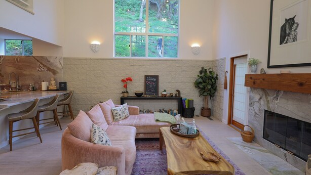 A spacious living area with a large window, a fireplace, a sofa, and a wooden coffee table.
