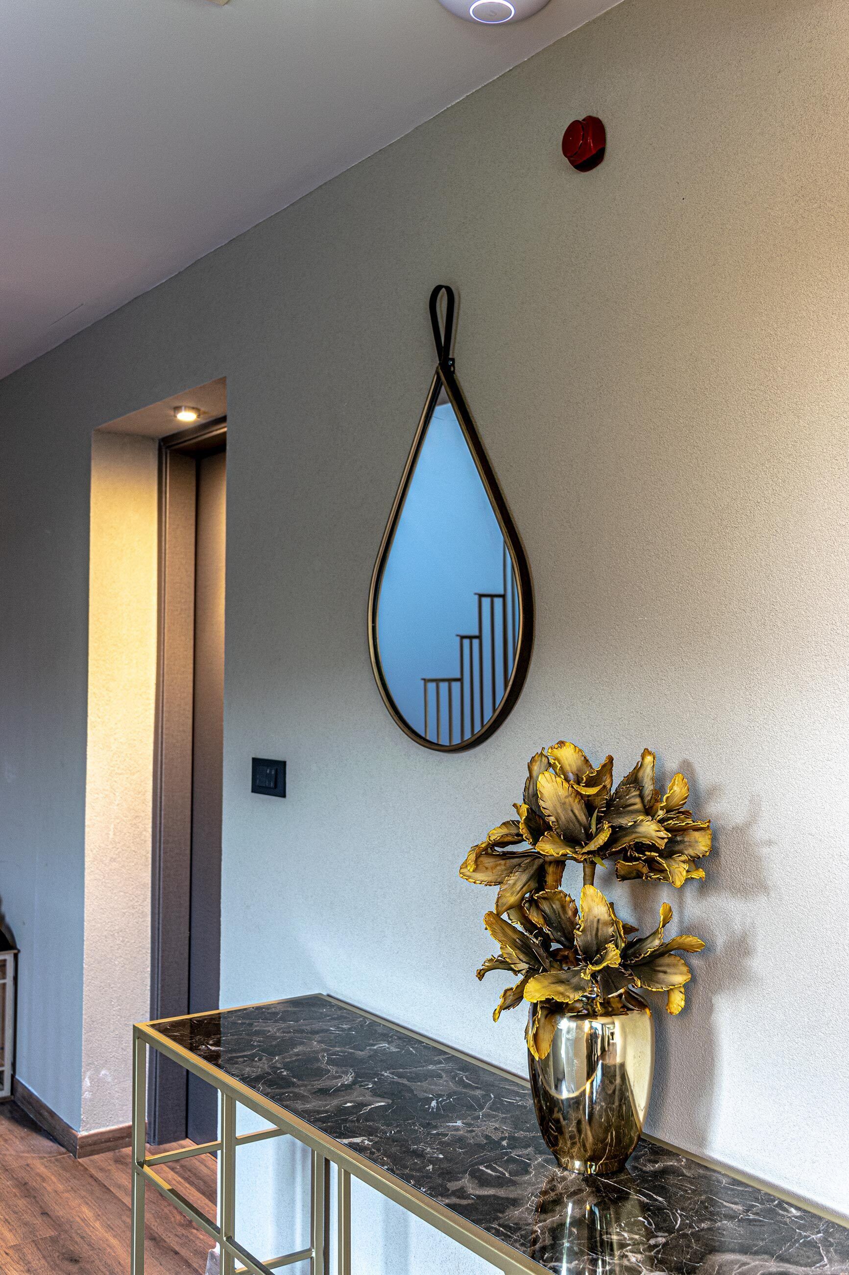 A hallway with a marble table, a vase with dried flowers, and a wall-mounted mirror reflecting a staircase.