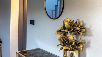 A hallway with a marble table, a vase with dried flowers, and a wall-mounted mirror reflecting a staircase.