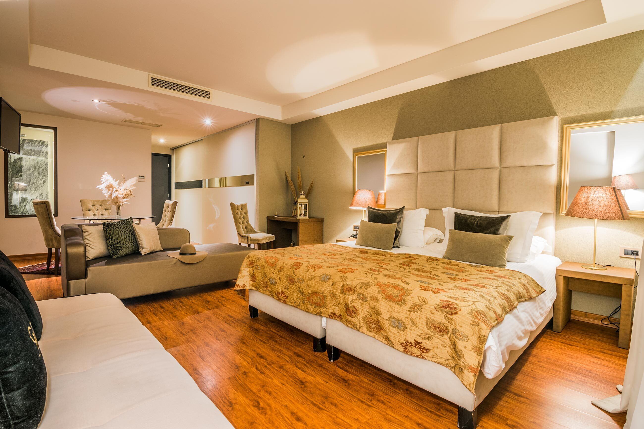 A modern hotel room with a large bed, a sofa, a desk, and a mirror.